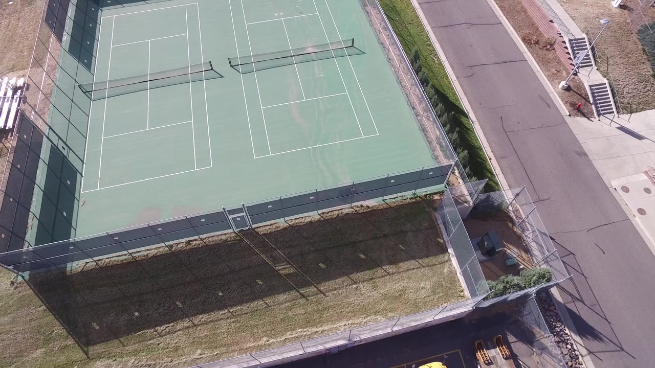 Aerial frame in Hidden Lake, Colorado with the fenced double tennis court shifted slightly across the view, bordered by a paved street and no visible people.