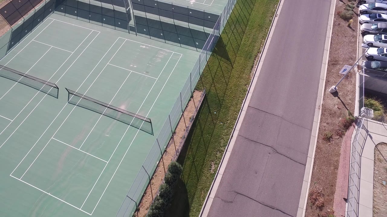 Top-down tennis courts next to a straight road and parking area.