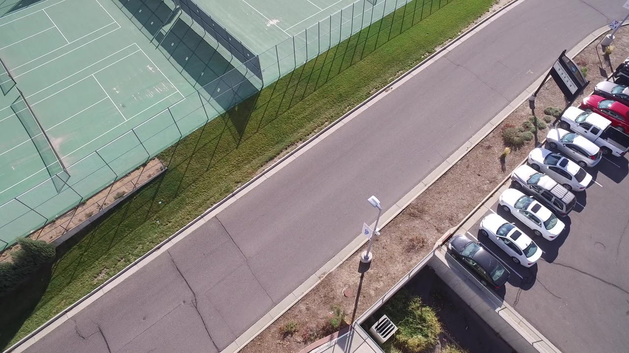 Overhead view of tennis courts, road, and parked cars.