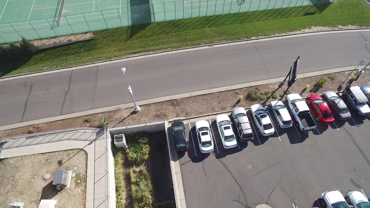 Overhead view of parked cars beside tennis courts and a road.