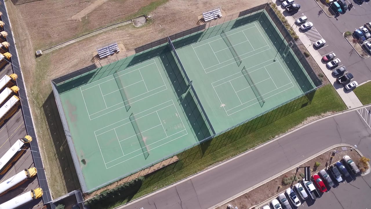 High aerial frame of tennis courts bordered by a parking lot and road.