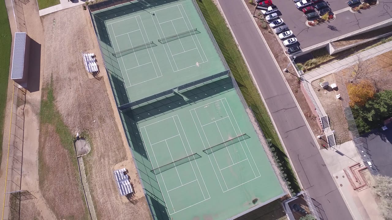 Overhead tennis courts next to a road, sidewalks, parked cars, and small buildings.