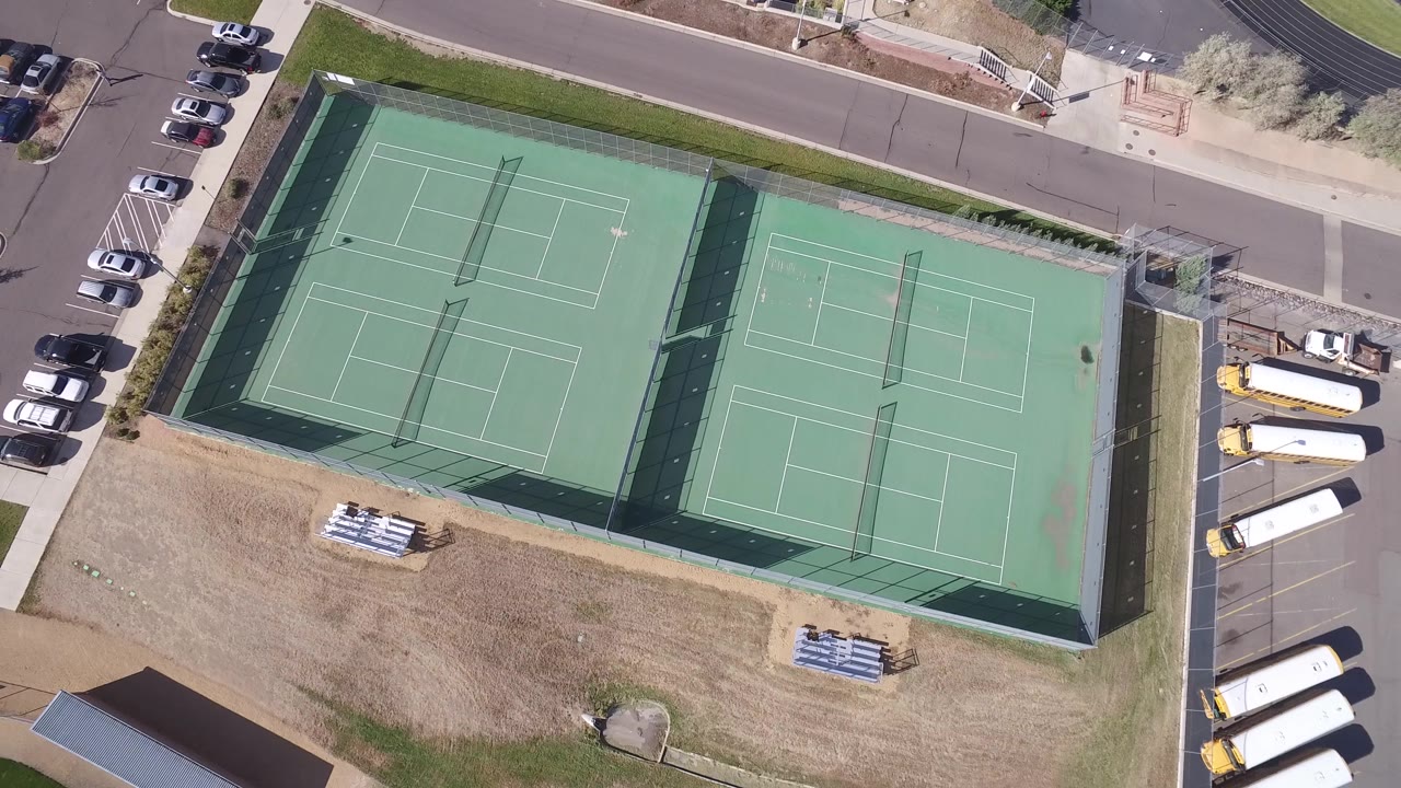Top-down view of tennis courts with buses parked along the lot.