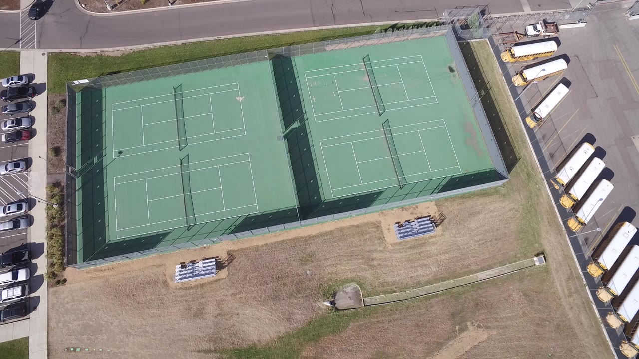 Hidden Lake, Colorado aerial frame keeps the tennis courts centered while school buses line the right edge and parked cars sit along the road above the courts.