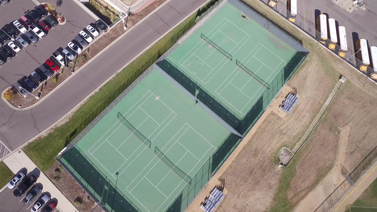 Overhead view of tennis courts beside a parking lot and road.