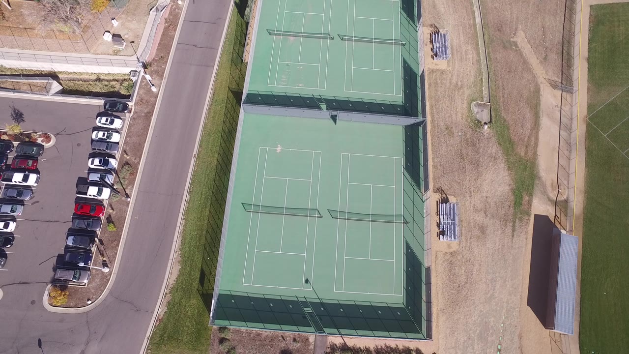 Overhead view of green tennis courts beside a parking lot and road.