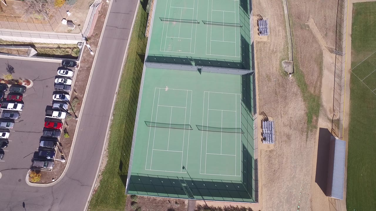 High aerial frame from Hidden Lake, Colorado with four green tennis courts centered beside a row of parked cars and no visible people.