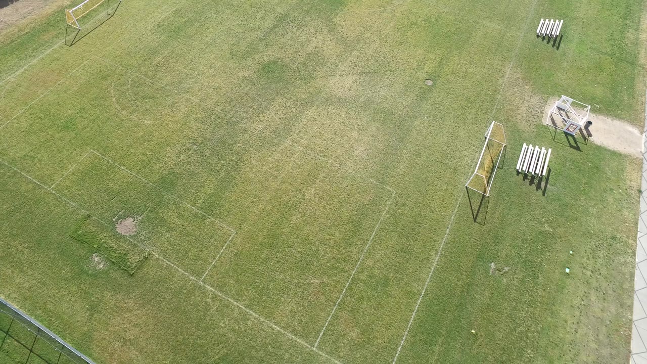 Aerial frame in Hidden Lake, Colorado with the field shifted slightly across the view, showing a goal near the right side, bench seating by the path, and no visible people.