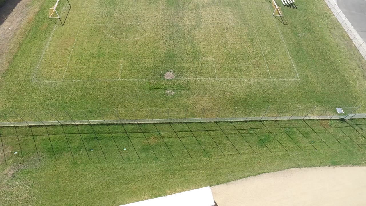 High aerial view in Hidden Lake, Colorado showing marked grass soccer fields, small goals, a fence line, and a pale road edge with no visible people.
