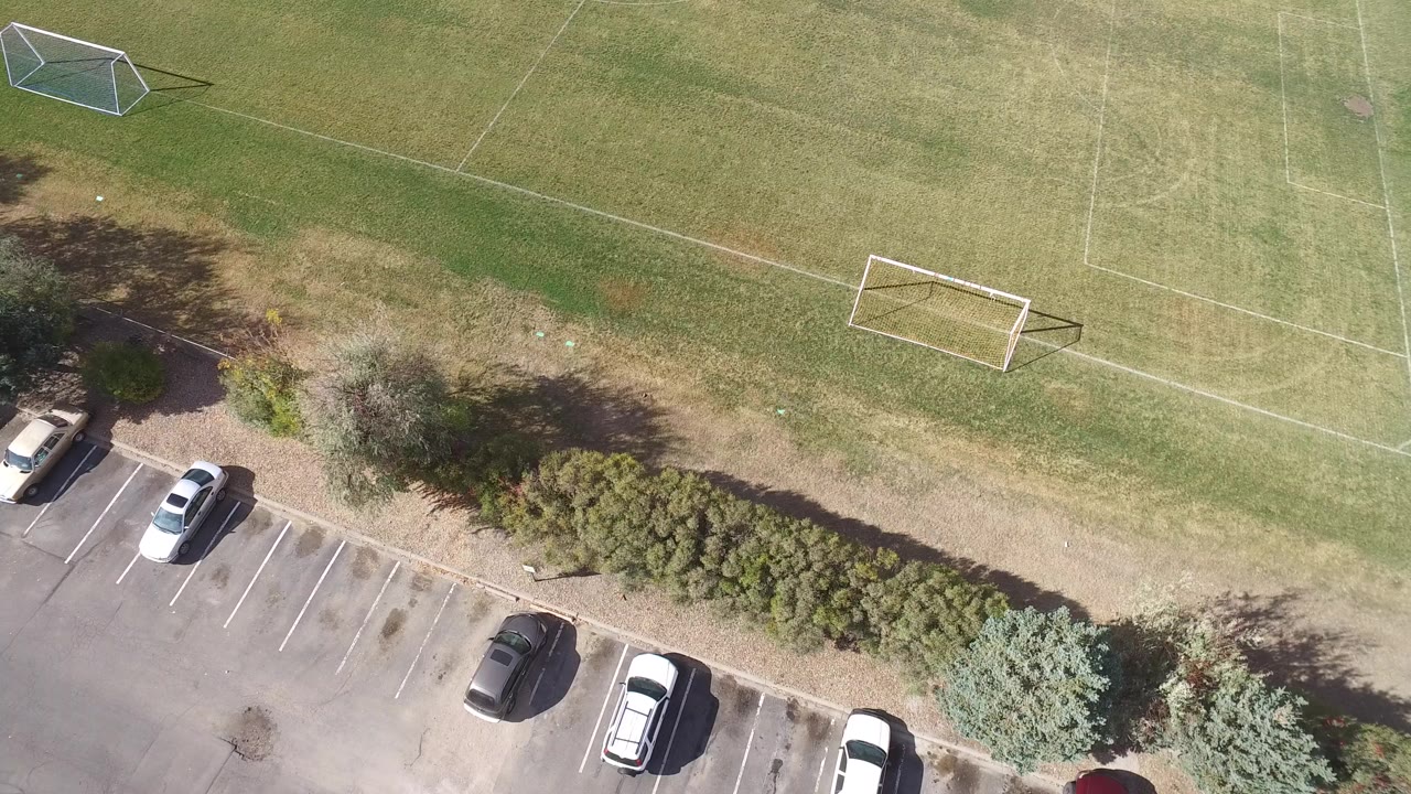 Overhead frame in Hidden Lake, Colorado showing a parking lot with scattered cars below shrubs and two soccer goals on grass, with no visible people.