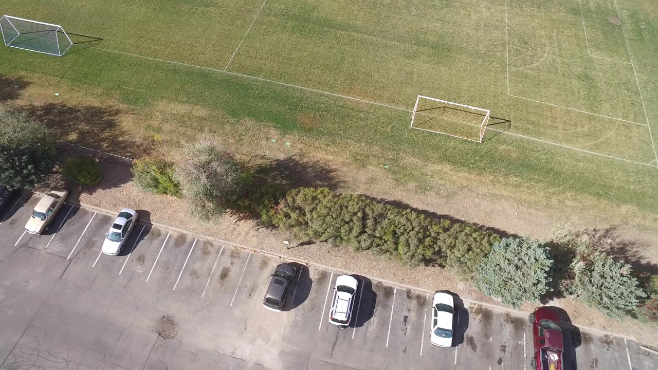 Drone view of parking stalls, cars, shrubs, and soccer goals.