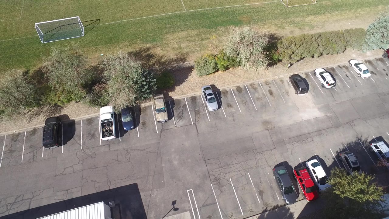 Aerial view in Hidden Lake, Colorado with the parking stalls and several vehicles centered below a tree border, and a soccer goal visible on the grass above, with no visible people.