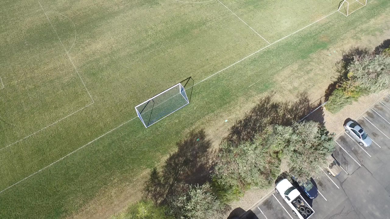 Overhead Hidden Lake, Colorado park frame with the soccer goal closer to center left, faint field lines across the grass, trees at the lot edge, cars, and no visible people.