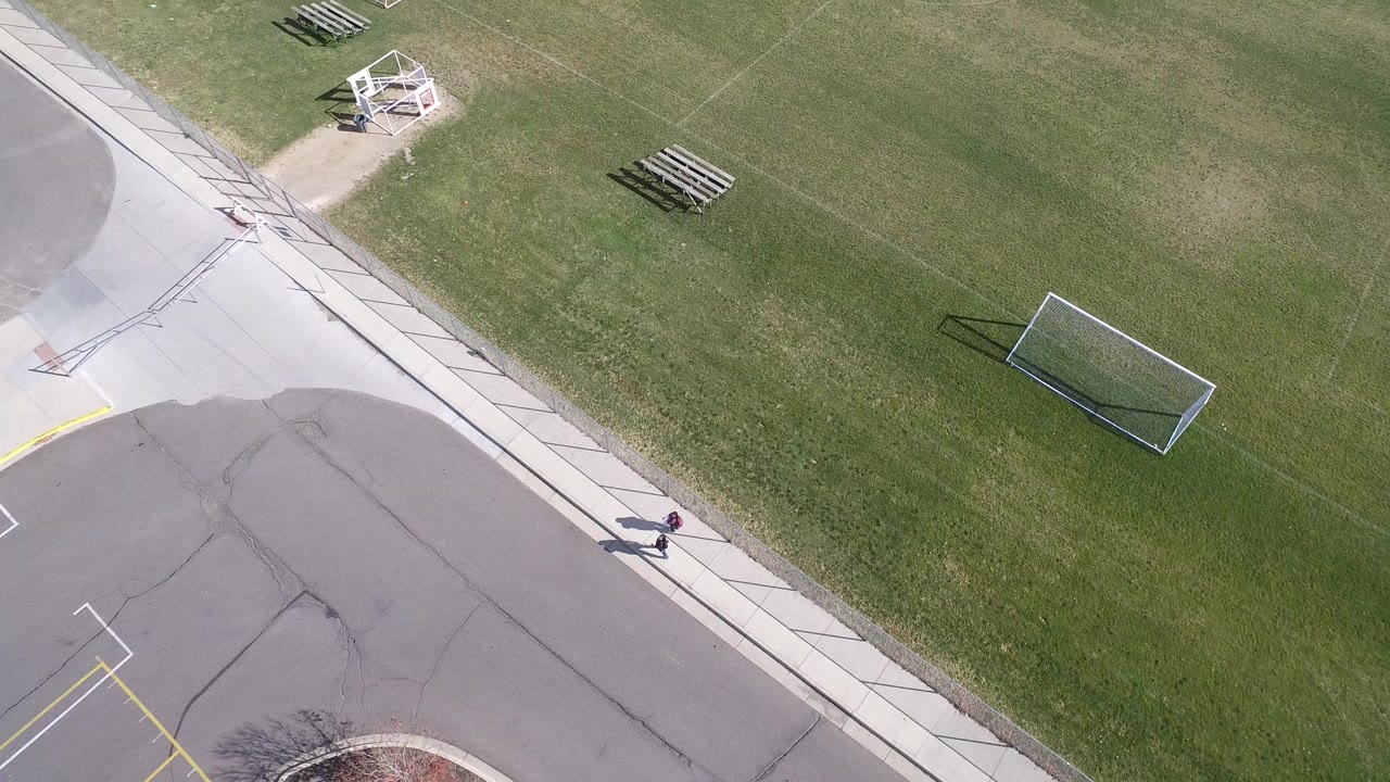Aerial view of a green field beside a paved road and sidewalk.