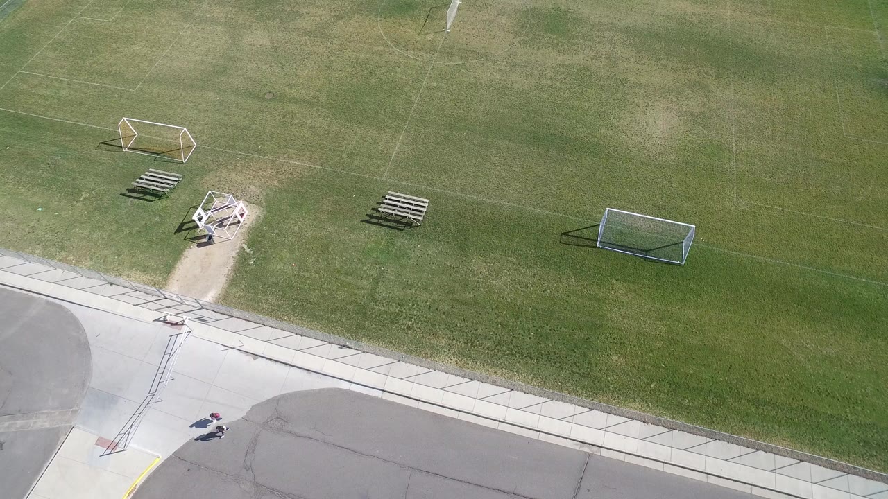 Aerial view of a grassy sports field with soccer goals and pavement edge.