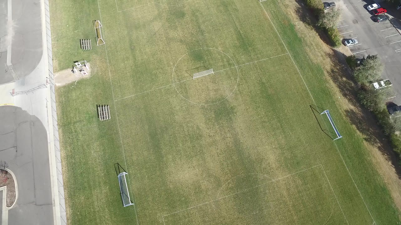 Aerial frame in Hidden Lake, Colorado with faint soccer-field lines across the grass, small goals at opposite areas, road pavement at the side, and no visible people.