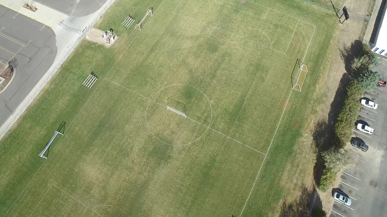 Overhead view of a grassy sports field beside a road and parking area.