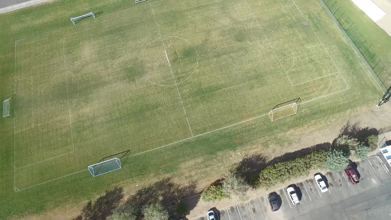 Overhead frame of worn soccer fields in Hidden Lake, Colorado, with small goals, faded field lines, trees, parked cars, and no visible people.
