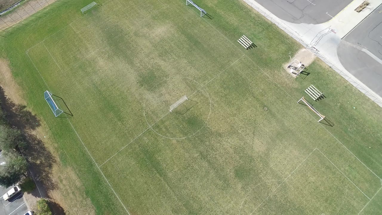 Top-down soccer field with bleachers, goals, and parking lot edge.