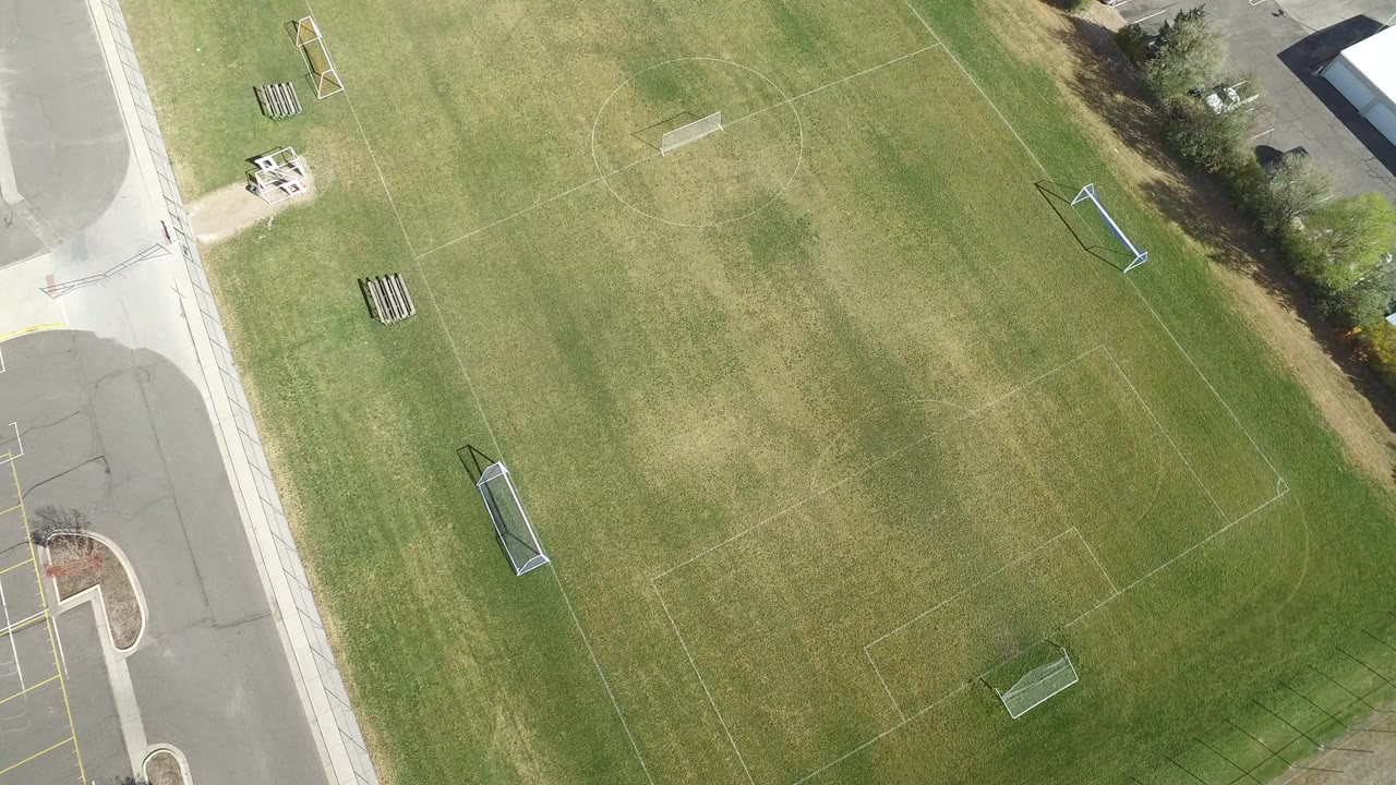 Overhead view of a grassy sports field beside roads and sidewalks.