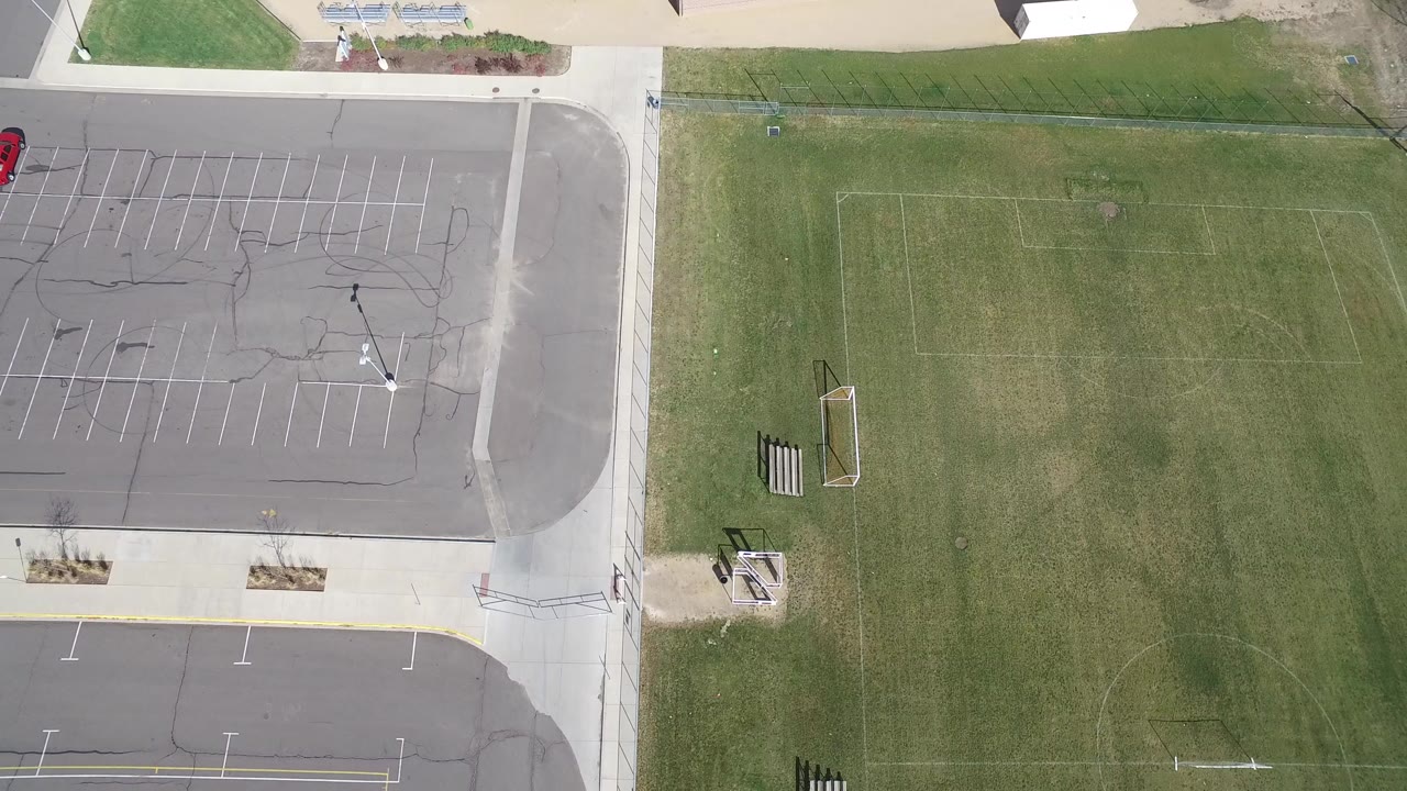 Overhead frame in Hidden Lake, Colorado showing an asphalt parking lot, sidewalk, grass sports field, goal frames, and no visible people.