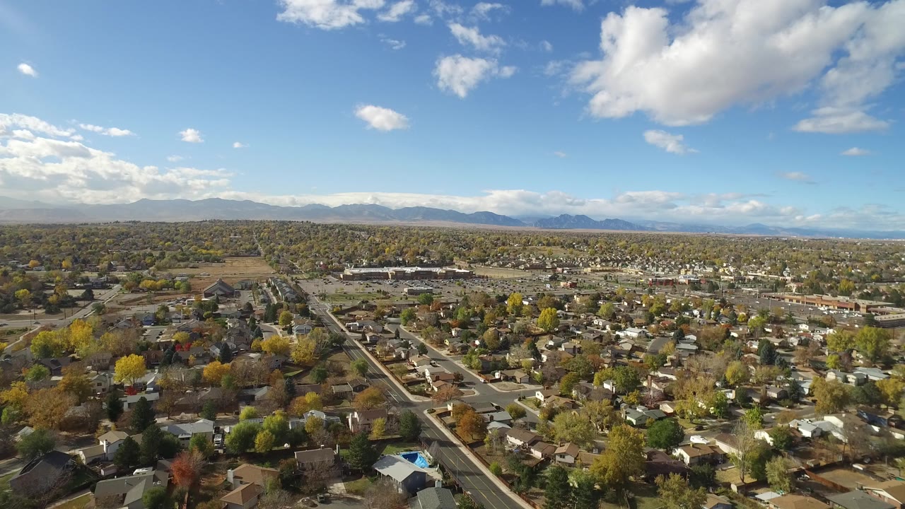 At 0:01, Hidden Lake, Colorado appears from above with gridded streets, many rooftops, autumn-colored trees, a large cloud overhead, and no visible people.