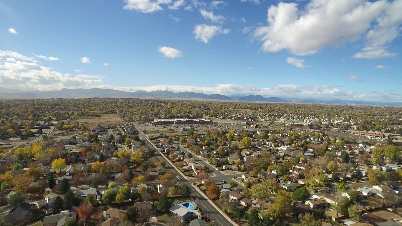 Drone-height view across homes, trees, roads, and a distant mountain range.