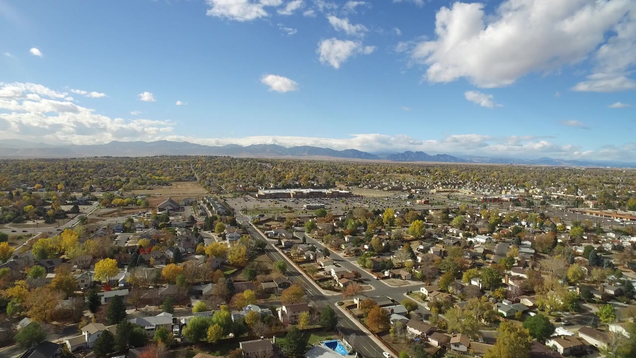 Aerial view over a residential town toward distant mountains under blue sky.