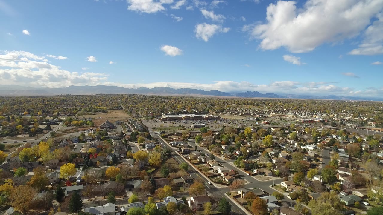 Aerial view over houses, streets, trees, distant mountains, and blue sky.