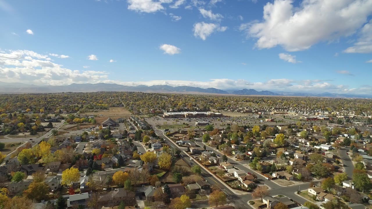 Aerial view of suburban roads, homes, trees, and distant mountains under blue sky.