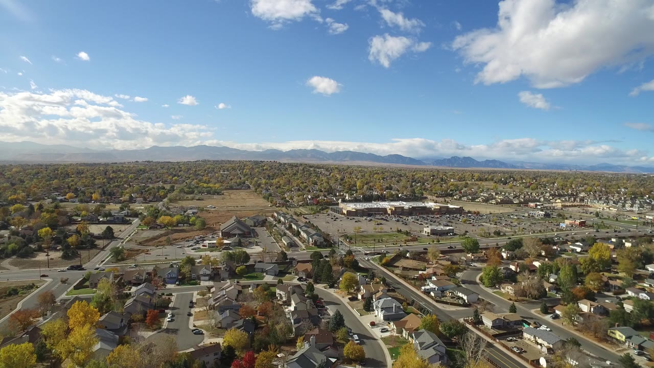 Opening aerial frame over Hidden Lake, Colorado showing residential streets, rooftops, autumn trees, commercial buildings, distant mountains, and no visible people.