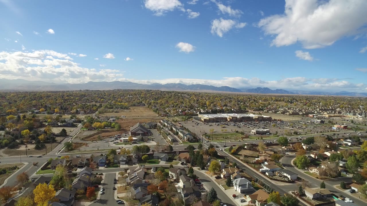 Aerial view over residential streets, parking lots, trees, and distant mountains