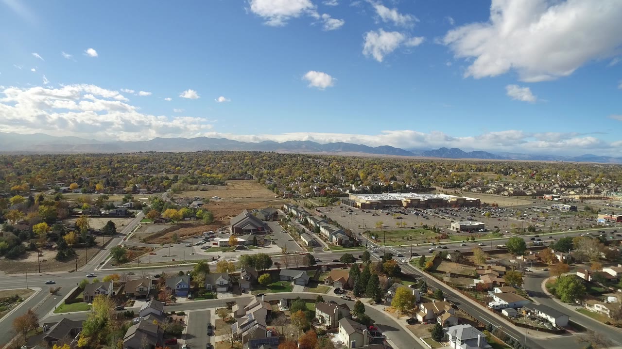 Aerial view of suburban roads, homes, trees, and distant mountains under a blue sky.