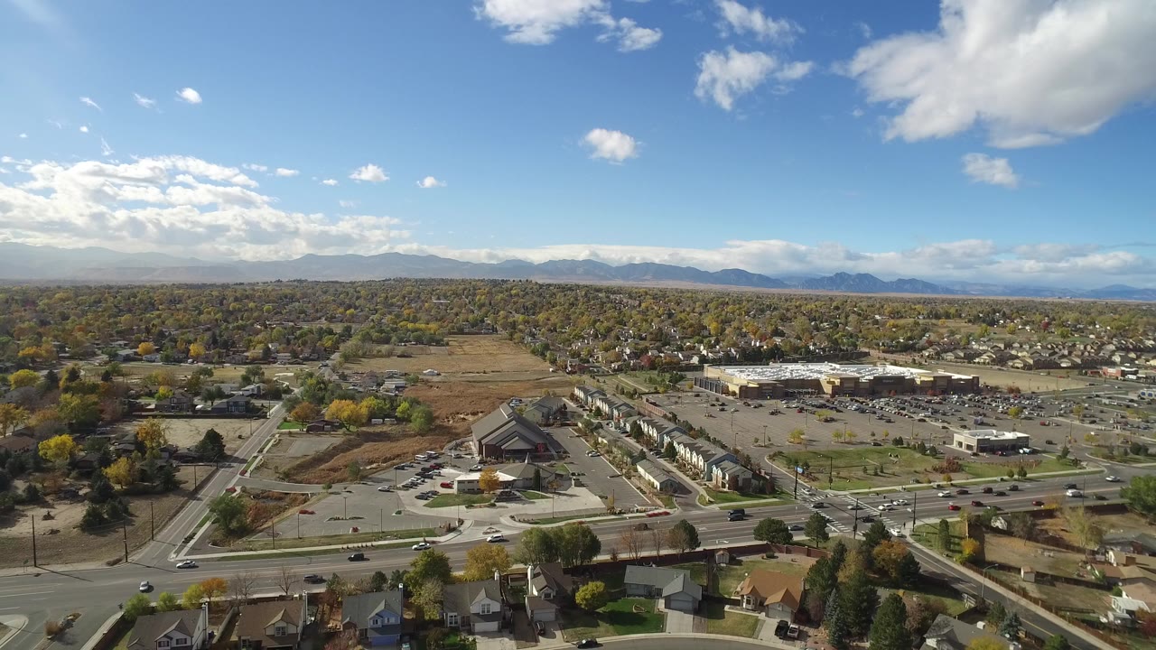 High aerial view over roads, homes, commercial buildings, and distant mountains.