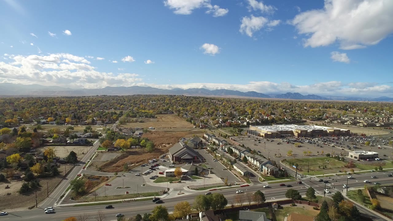 Aerial view of suburban roads, parking lots, homes, and distant mountains under a blue sky.