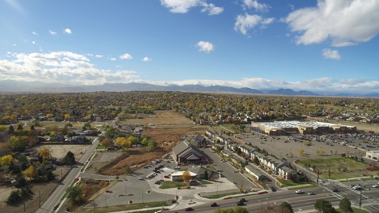 Aerial frame in Hidden Lake, Colorado looking across open parcels, clustered homes, a large parking area, tree-lined blocks, distant mountains, and no visible people.