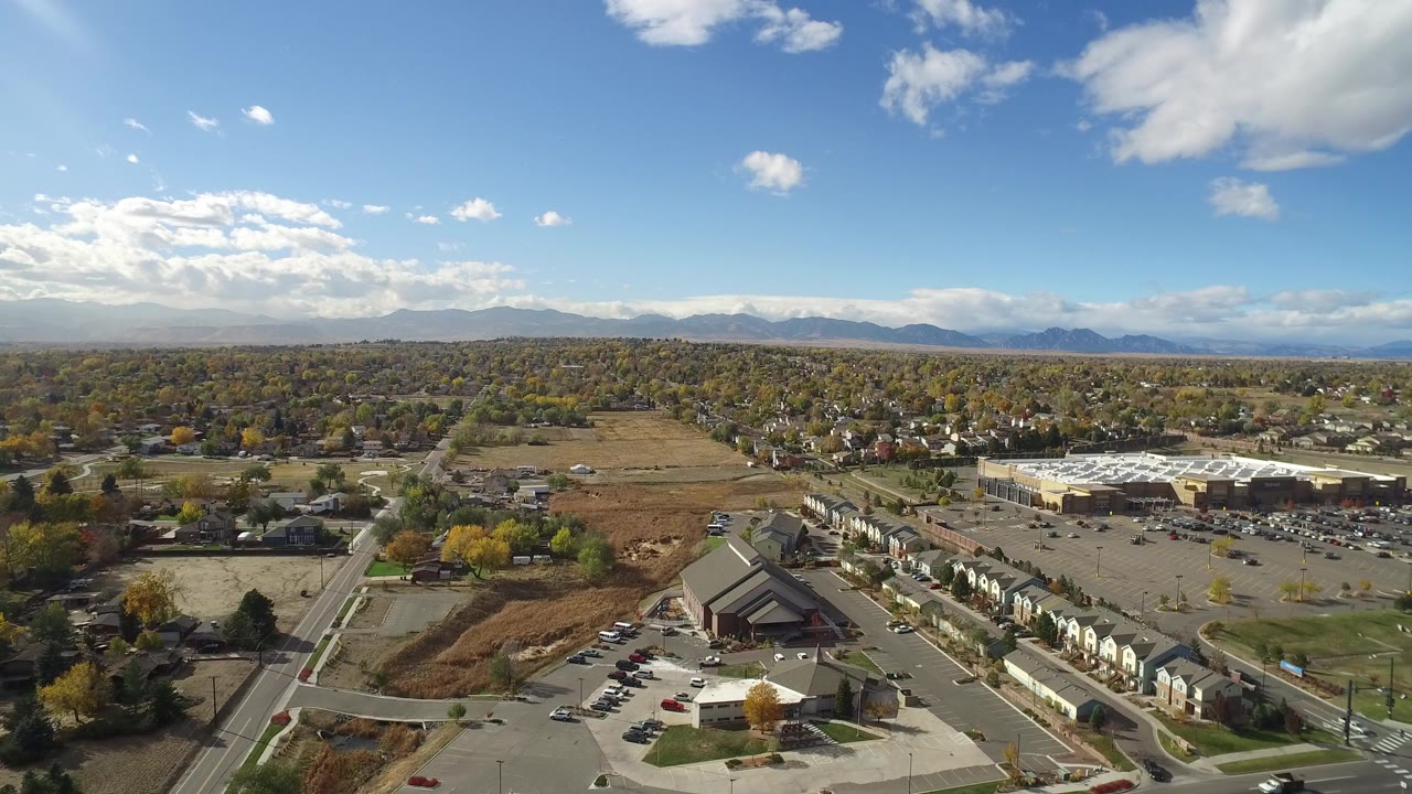Aerial view over roads, parking lots, homes, open fields, and distant mountains.