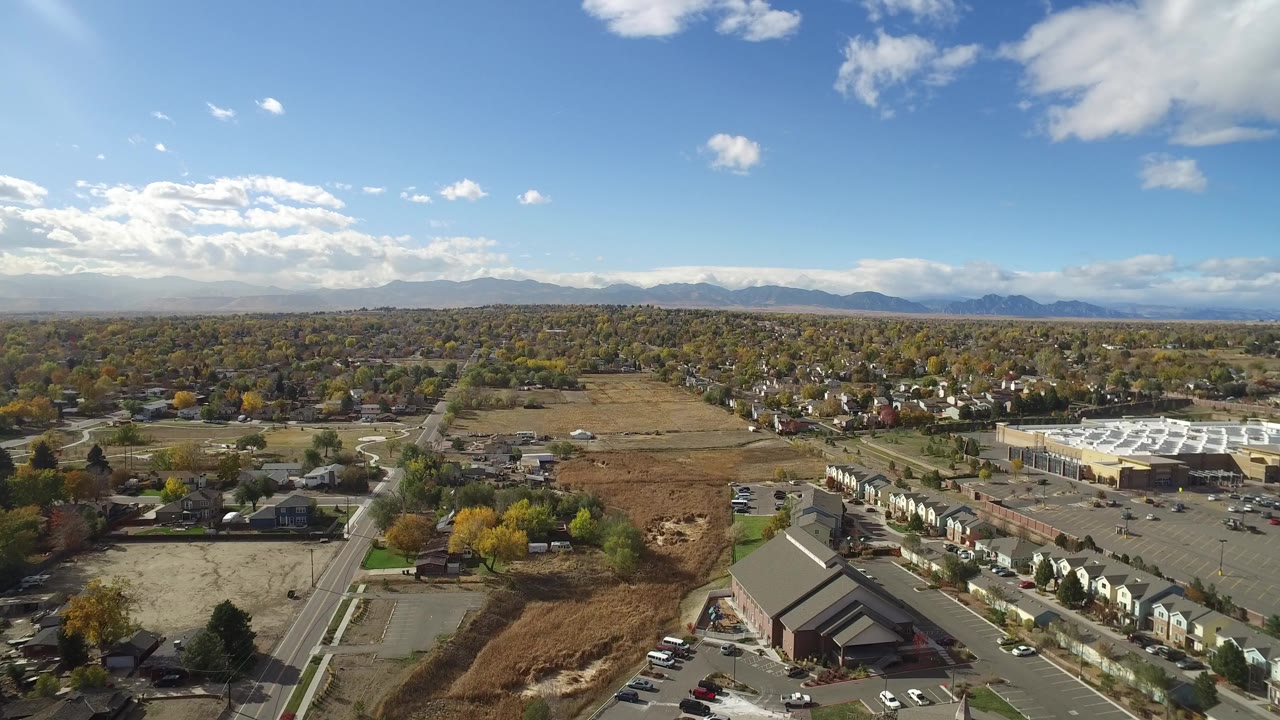 Opening aerial frame over Hidden Lake, Colorado, showing roads, open fields, residential blocks, autumn trees, distant mountains, and no visible people.