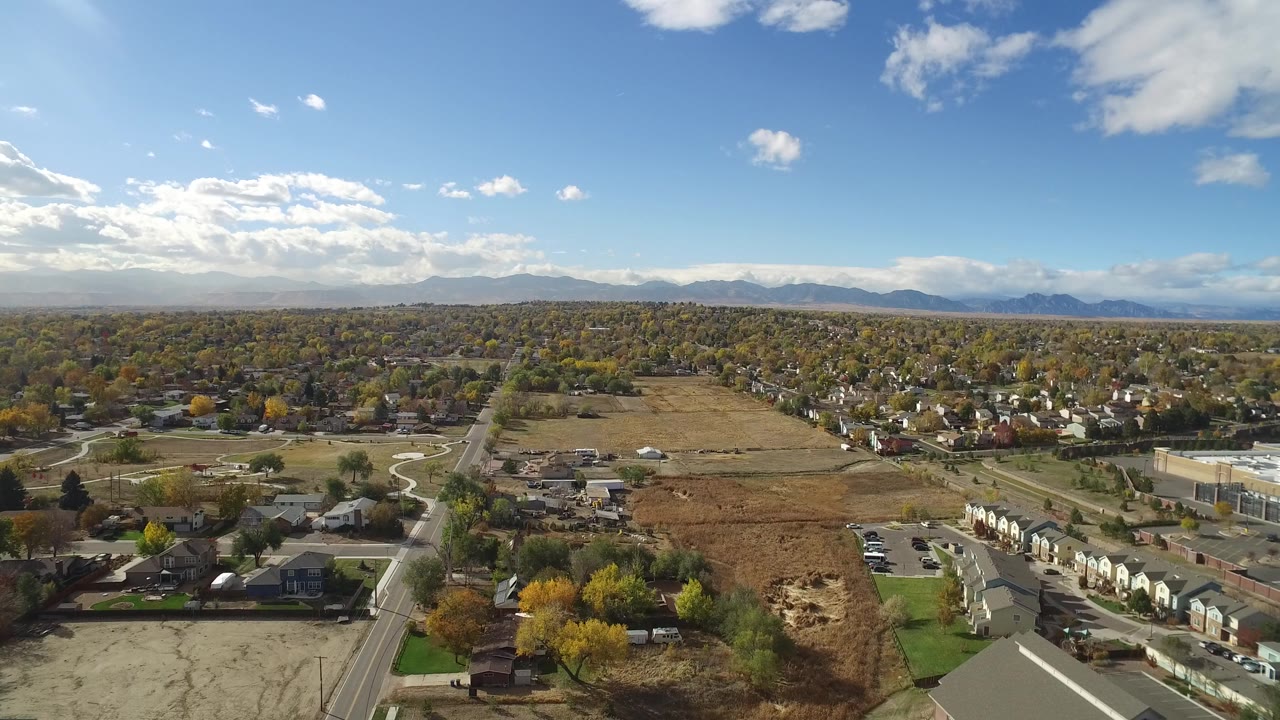 Elevated neighborhood view with a road, homes, brown field, and distant mountain range.