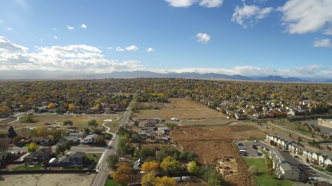 Wide aerial view over Hidden Lake, Colorado with residential streets, open brown fields, scattered autumn trees, distant mountains, and no visible people.