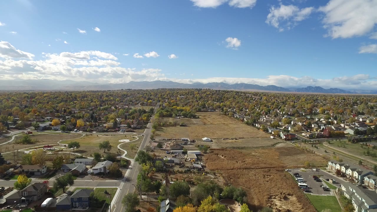 Aerial view of suburban homes, roads, open field, trees, and distant mountains.