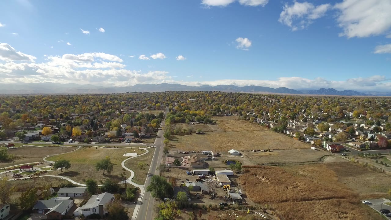 Aerial view over a road, fields, homes, trees, and distant mountains.