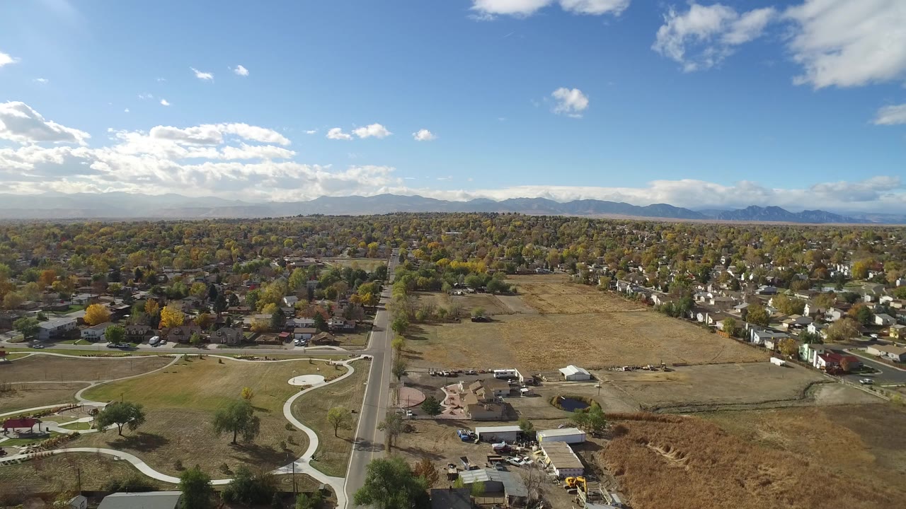 Aerial view over a road, open fields, houses, trees, and distant mountains.