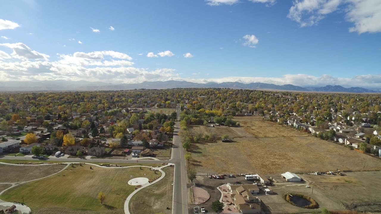 Drone-height view of a residential edge, open grass, curved paths, and a mountain skyline.