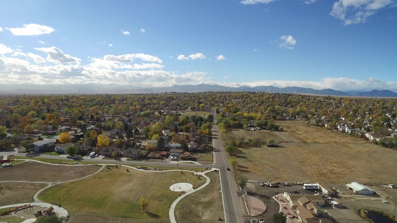 Aerial view of park paths, a road, homes, fields, mountains, and blue sky.