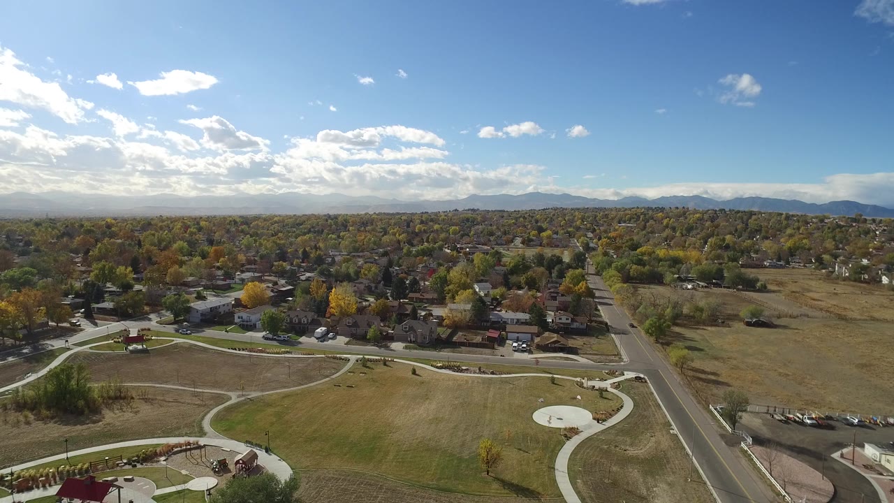 Wide aerial view of park paths, houses, trees, road, fields, sky, and distant mountains.