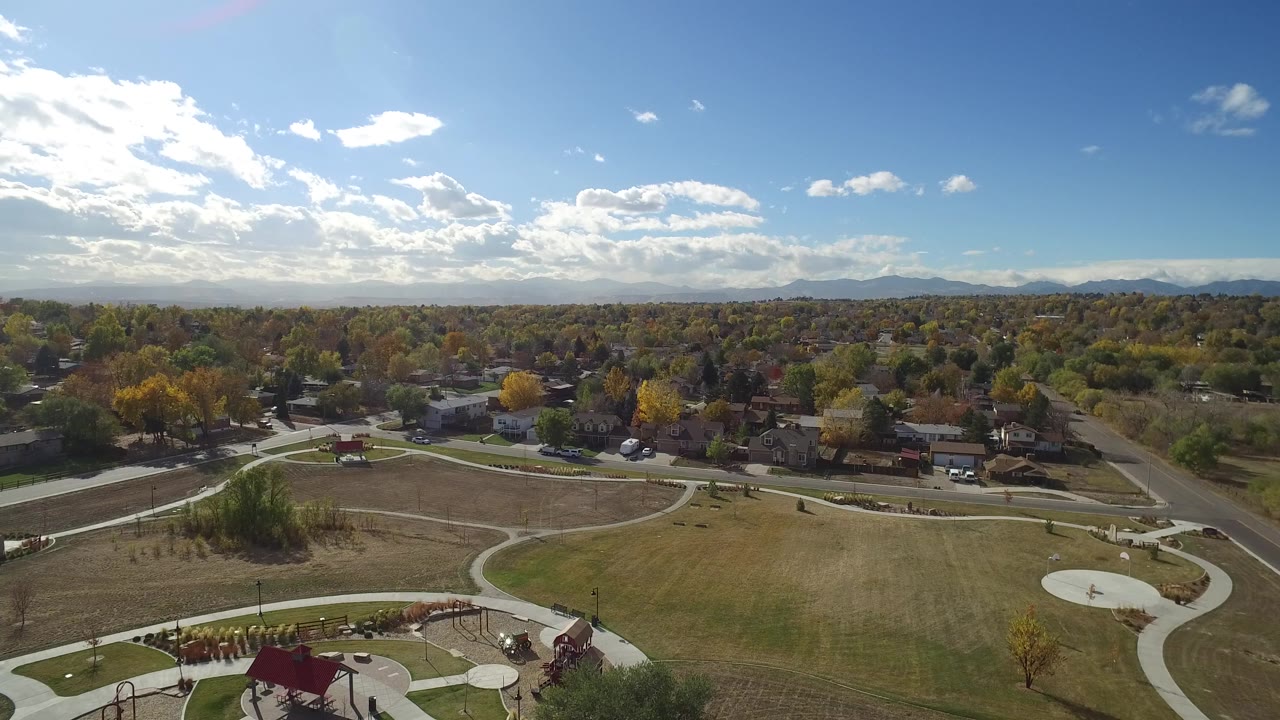Hidden Lake, Colorado aerial frame with open grass and intersecting paths in the foreground, a row of homes and trees in the midground, hazy mountains on the horizon, and no visible people.