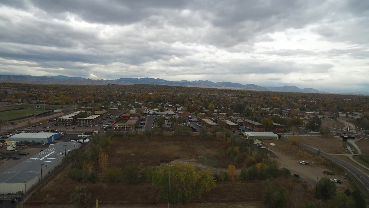 Aerial view over sheds, dry lots, roads, and distant mountains under gray clouds.