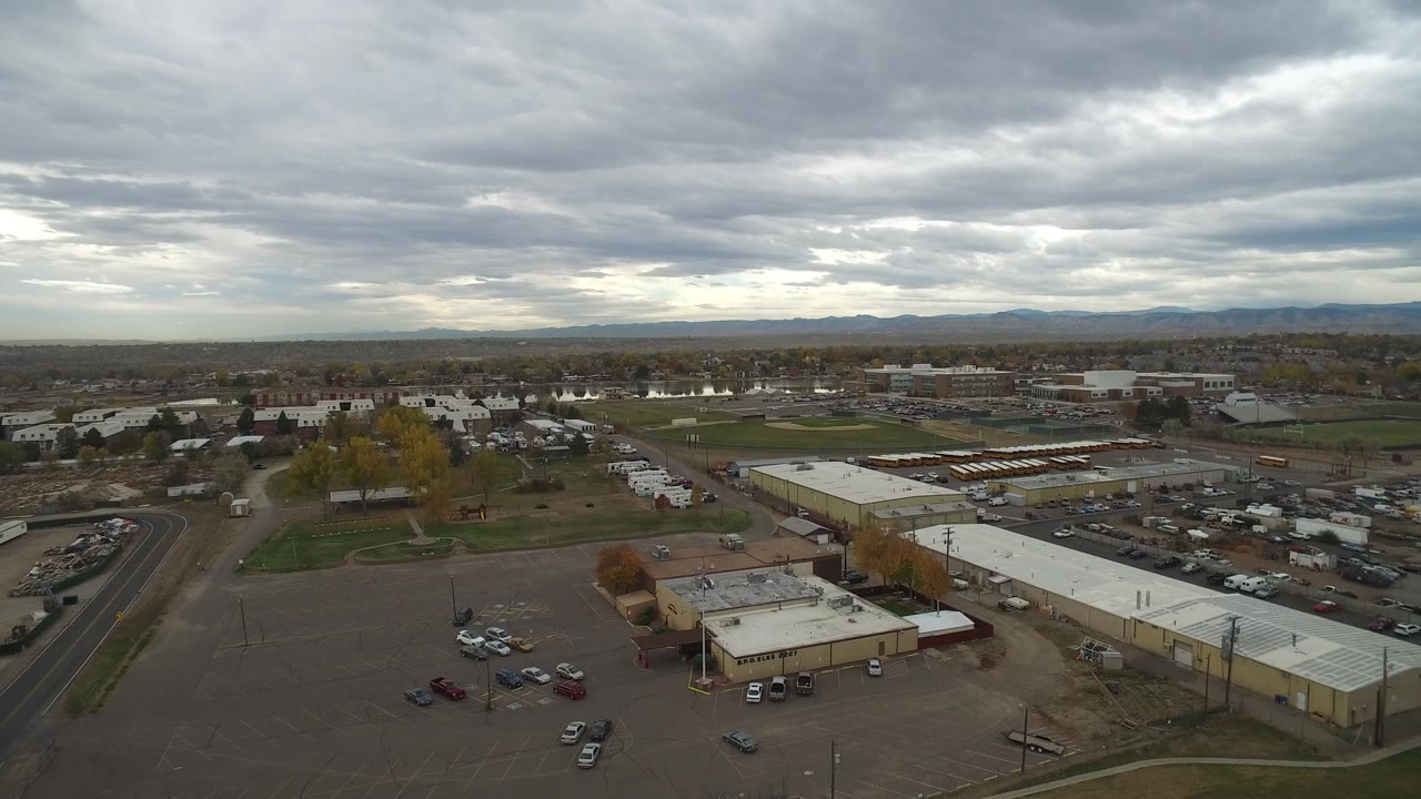 Elevated town panorama with parking areas, roadside buildings, trees, and gray clouds.