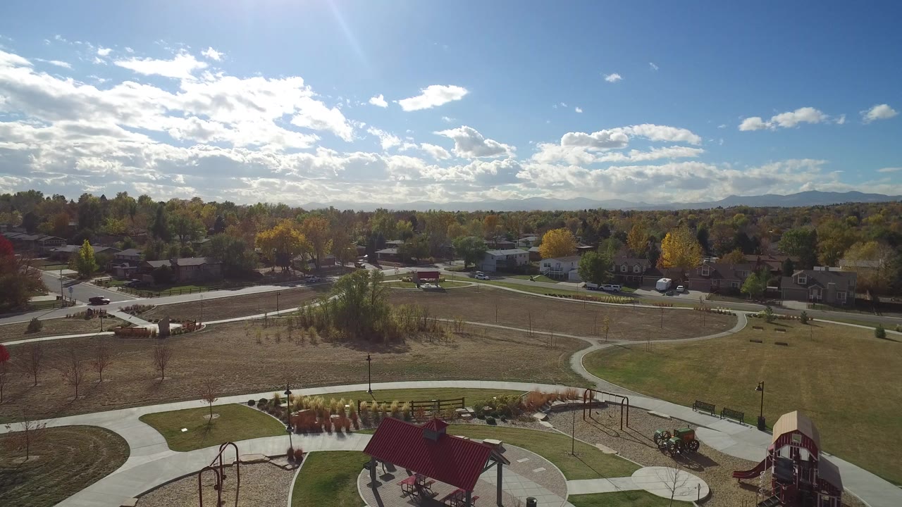 Second frame over Hidden Lake, Colorado, with the red-roofed shelter lower in frame, a playground at right, curving walkways, residential streets, fall-colored trees, distant hills, and no visible people.